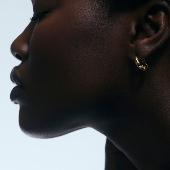 Close-up of a person wearing gold hoop earrings against a light background