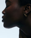 Close-up of a person wearing gold hoop earrings against a light background