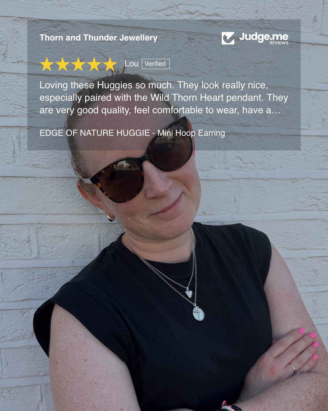 Woman wearing sunglasses and a black top with a white brick wall background